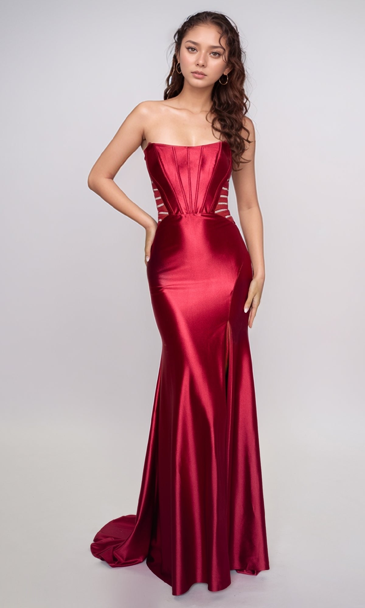 A woman stands in the Nina Canacci 5307 long formal dress—a strapless, floor-length red satin gown with corset-style detailing, a fitted silhouette, and loose wavy hair.